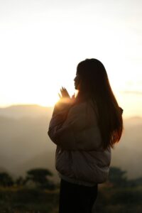 A woman standing outside at sunrise in a jacket, appearing peaceful, grounded, and connected to calm awareness.