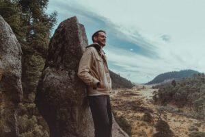 A man standing near a rock overlooking a valley symbolizes perspective, clarity, and emotional grounding.