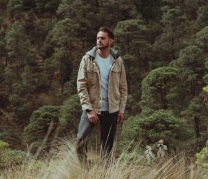 A man standing among tall trees, reflecting calm presence, grounding, and connection to the natural environment.