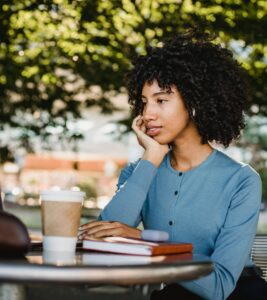 An African American woman is sitting with a book and coffee, reflecting calmly in a thoughtful and introspective moment.