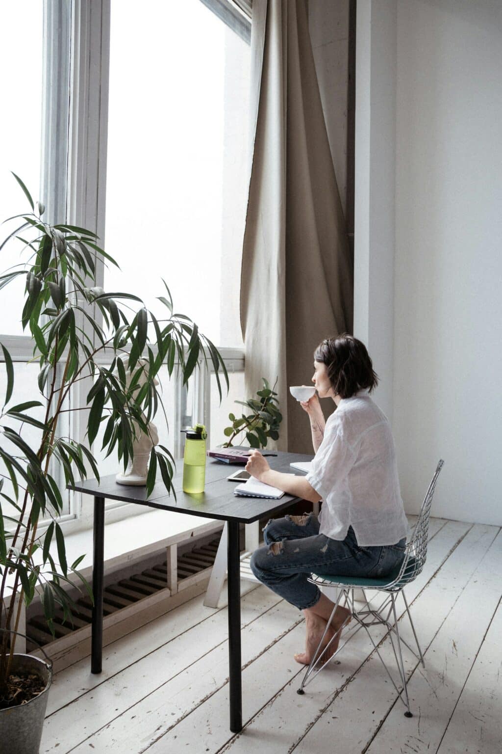 woman in white top sitting on chair in front of big window