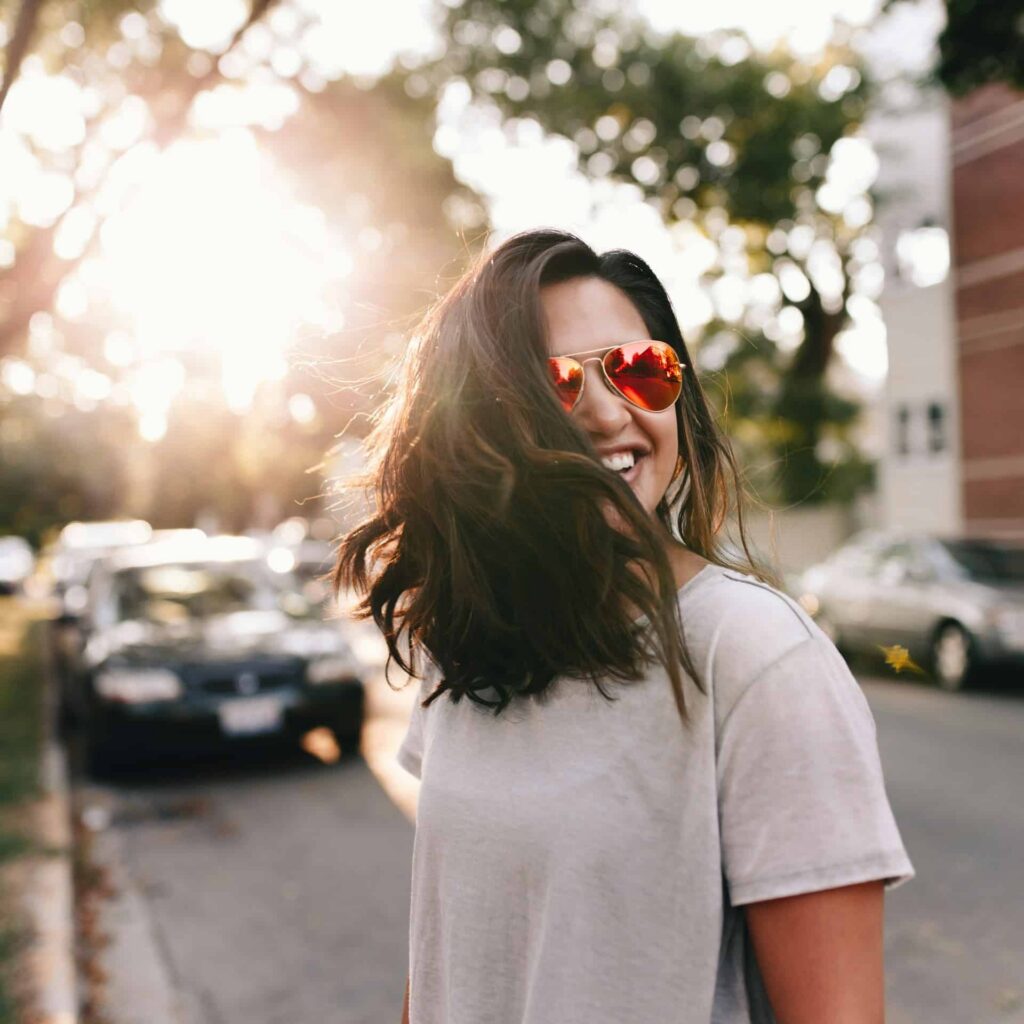 A woman standing by a window, smiling, represents hope, emotional relief, and a sense of renewed well-being.