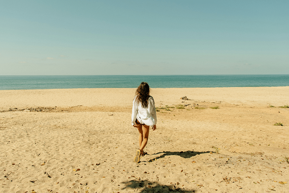 a woman walking across a sandy beach next to the ocean